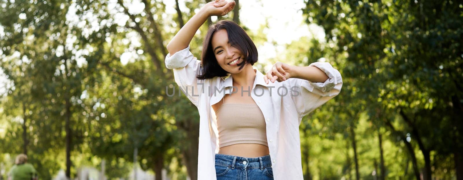 Carefree woman dancing and walking in park with hands lifted up high, smiling happily. Lifestyle concept by Benzoix