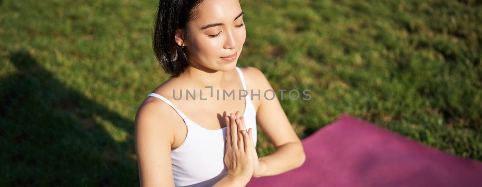Portrait of young mindful woman, practice yoga, exercising, inhale and exhale on fresh air in park, sitting on rubber mat by Benzoix