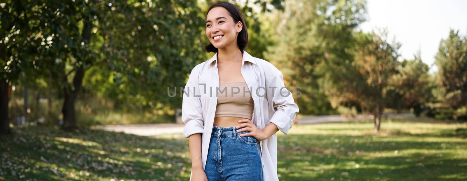 Happy asian girl walking in park, feeling freedom and joy, walking outdoors on sunny day.