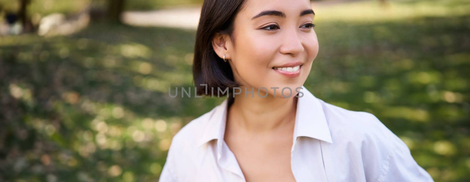 Beautiful young asian girl smiling, laughing and walking along park, enjoying summer sunny day. People and lifestyle concept