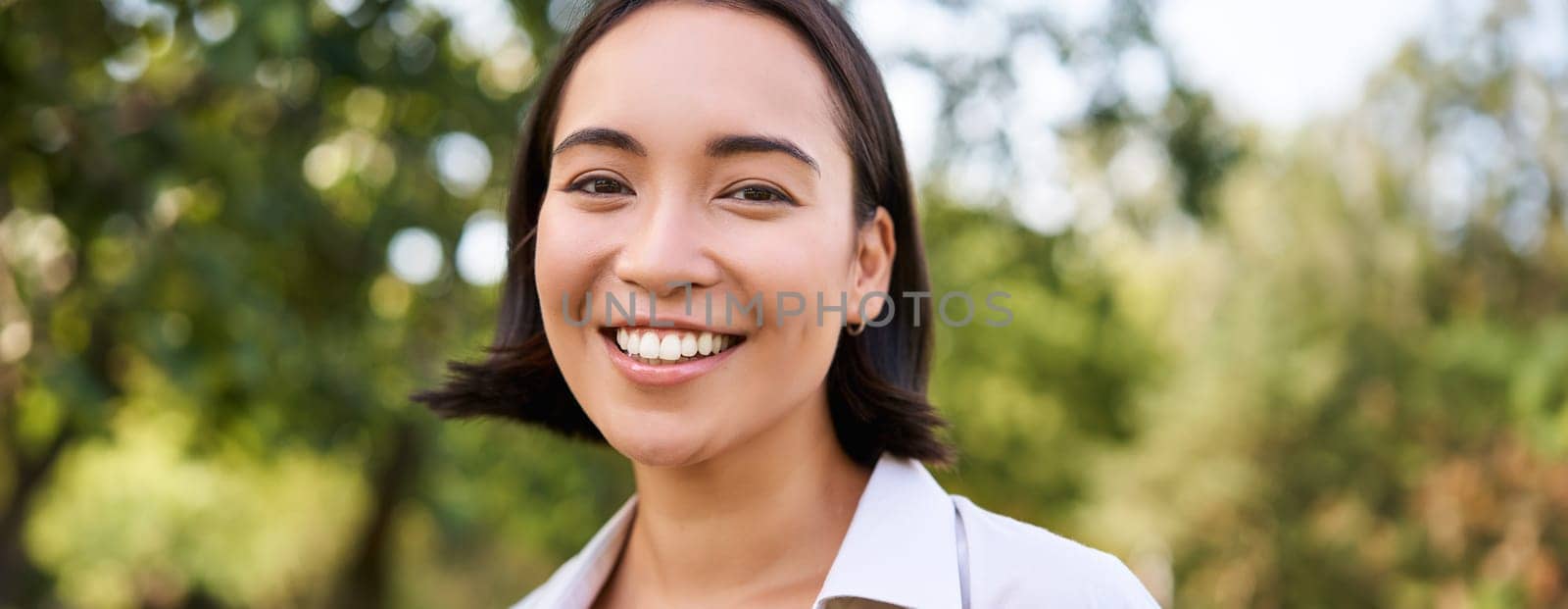 Close up face of asian happy girl, smiling and looking at camera carefree, walking in park.