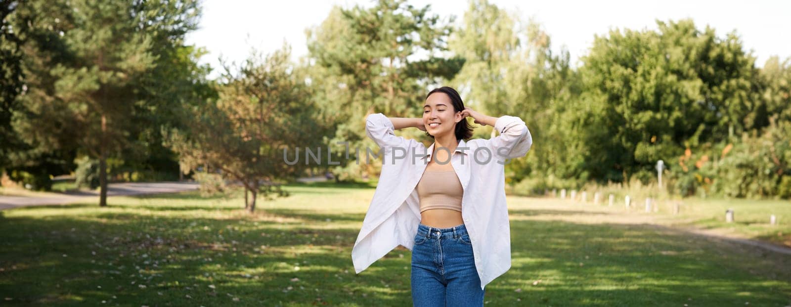Carefree asian girl laughing and dancing in park, enjoying summer sunny day, raising hands up and breathing fresh air by Benzoix