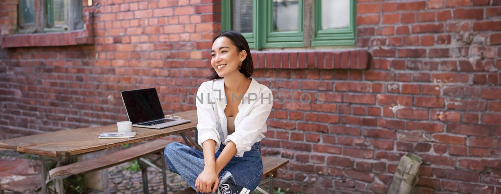 Vertical shot of trendy asian girl sitting in cafe alone with laptop, working or studying, browsing on computer. People and lifestyle concept