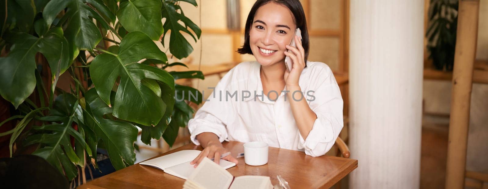 Smiling woman talking on mobile, answer phone call and looking happy, sitting in cafe. People and lifestyle concept