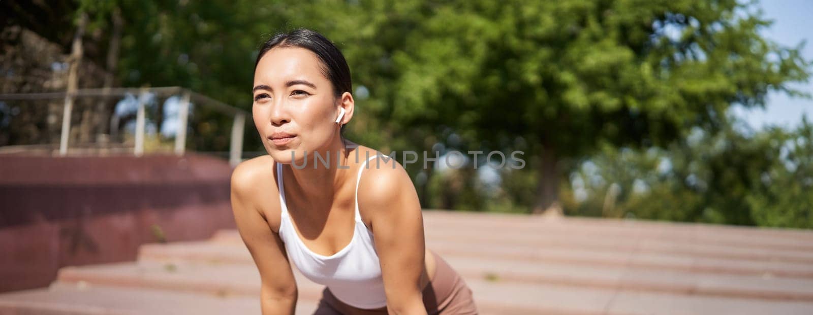 Portrait of asian woman taking break, breathing heavily and panting after running, jogger standing and wiping sweat off forehead, smiling pleased.