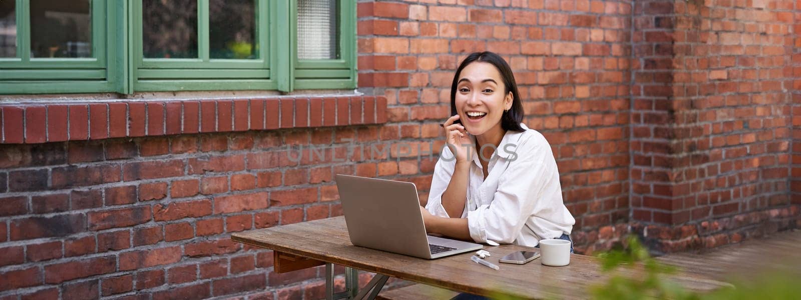 Enthusiastic asian woman sitting with laptop, laughing and smiling, looking happy, working remote online.