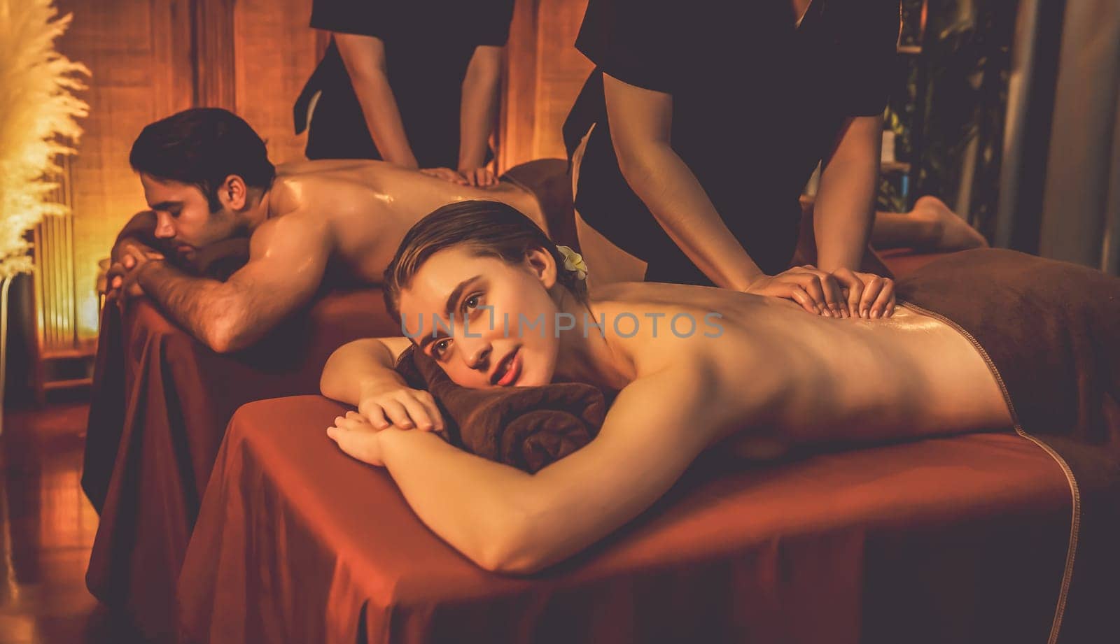 Caucasian couple customer enjoying relaxing anti-stress spa massage and pampering with beauty skin recreation leisure in warm candle lighting ambient salon spa at luxury resort or hotel. Quiescent