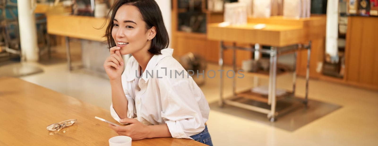 Portrait of beautiful asian woman with smartphone, relaxing in cafe, sitting and enjoying coffee while using mobile phone.