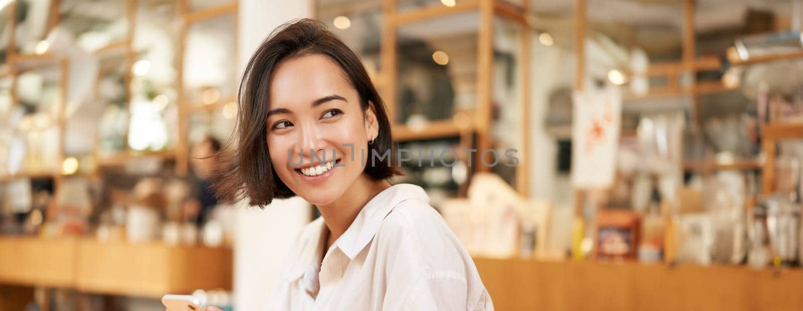 Portrait of young brunette woman, sitting with coffee and using smartphone in a cafe, chatting on mobile phone.