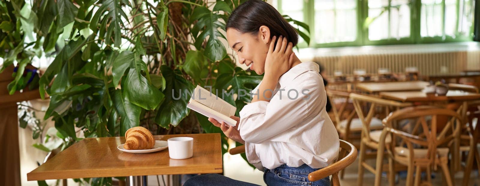 Tender, beautiful asian girl sitting with a book in cafe, reading and drinking coffee. People and lifestyle concept.