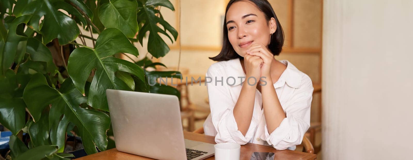 Beautiful brunette girl with laptop, sitting in cafe, working remotely, freelancing while sitting in coworking space.