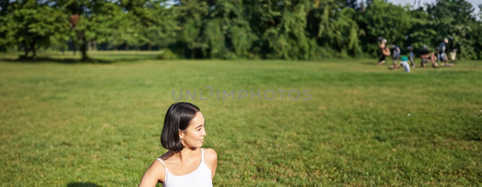 Woman meditating in park on rubber mat, sitting on green lawn and practice yoga, concept of sport and wellbeing.