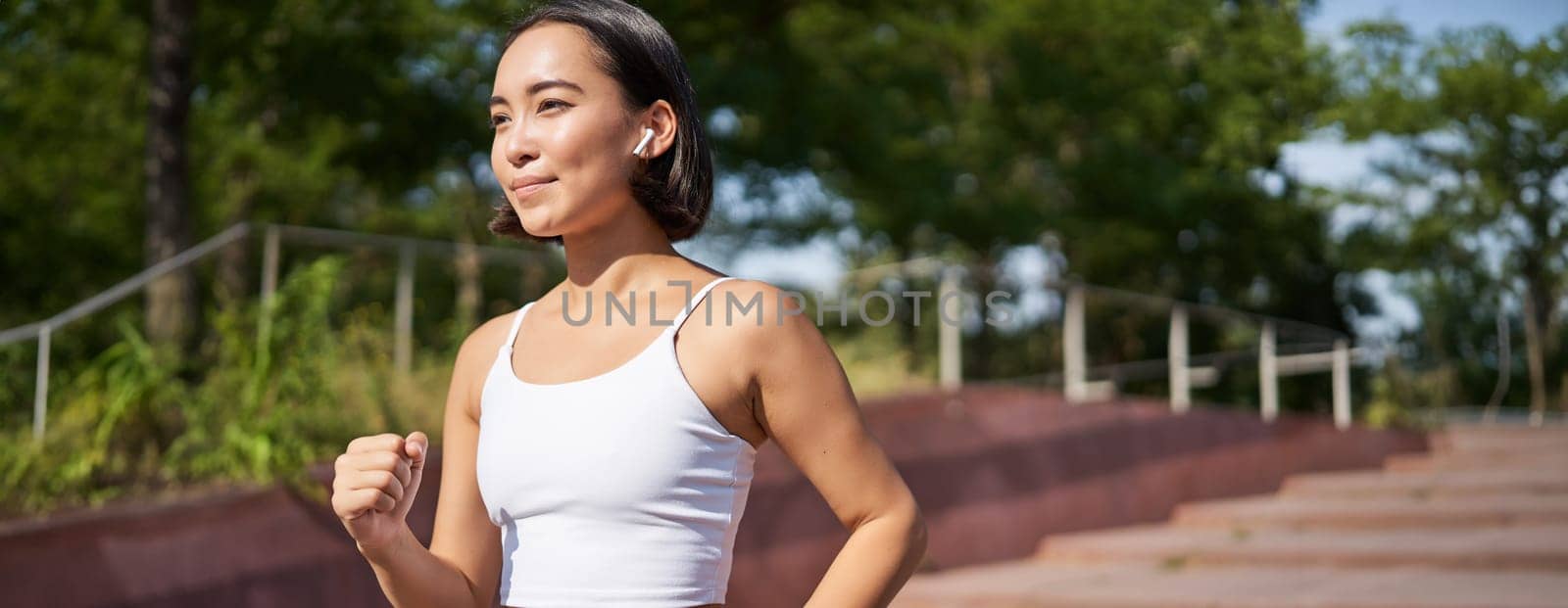 Wellbeing and sport. Asian fitness girl runner, jogging in park, running on street in leggings, smiling happily by Benzoix