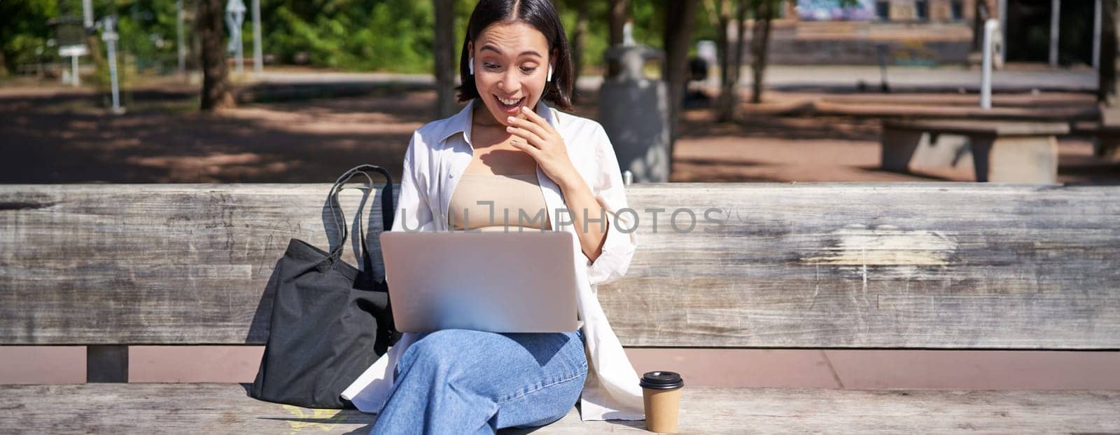 Young asian woman talking on video chat with laptop, sitting on bench, having online conference on remote. Copy space