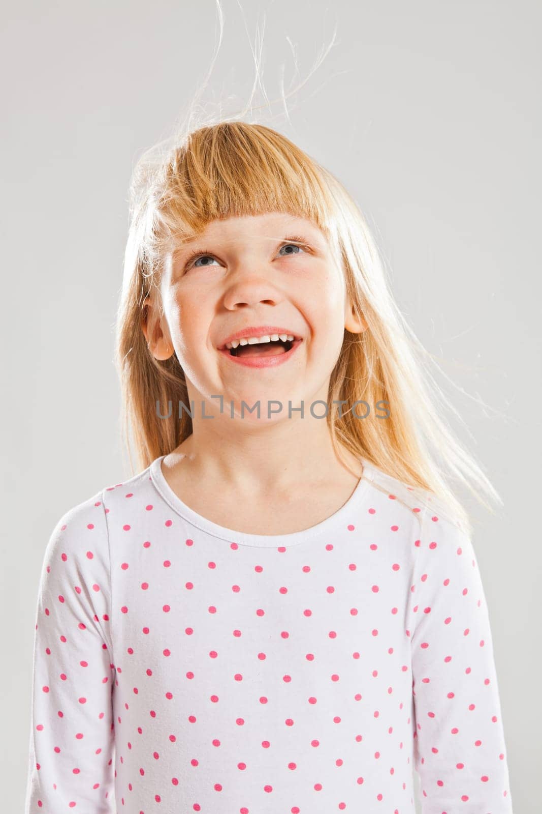 Studio portrait of happy smiling young girl looking up with wind blowing her hair