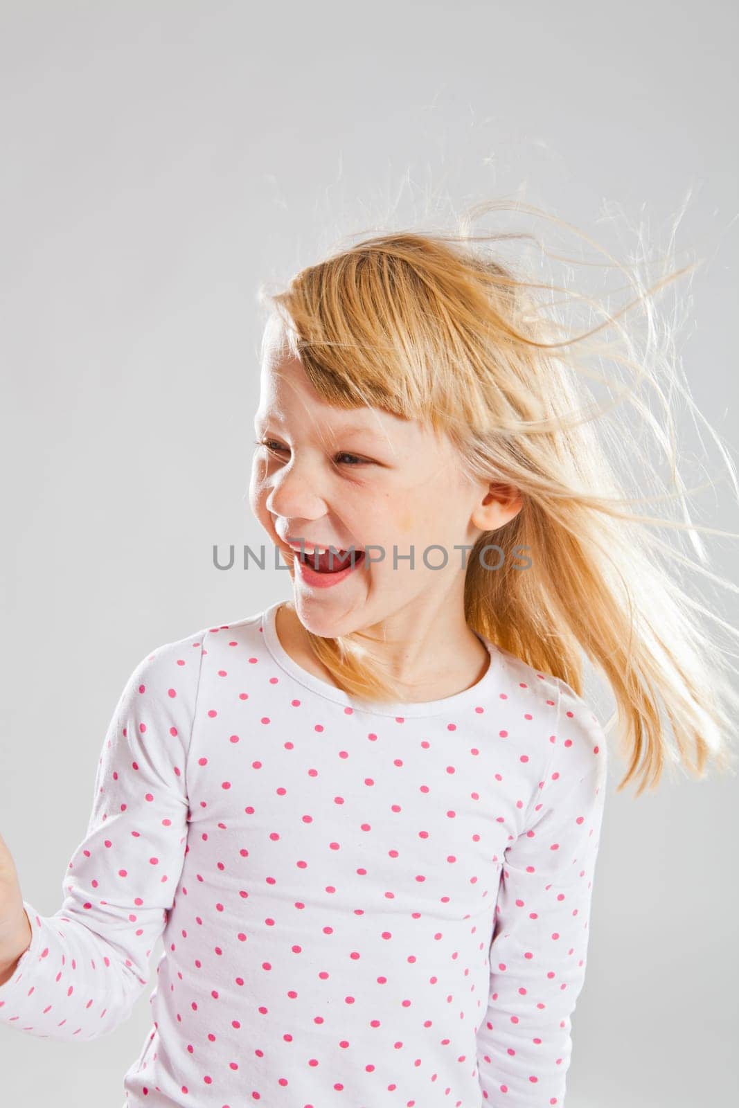 Studio portrait of happy smiling young girl with wind blowing her hair