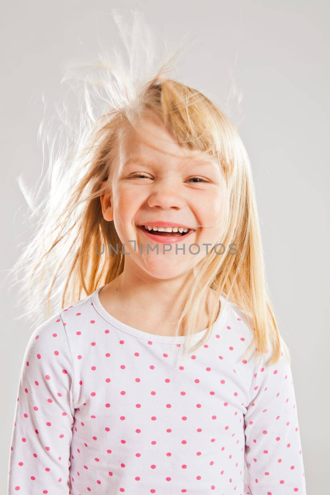 Studio portrait of happy smiling young girl with wind blowing her hair