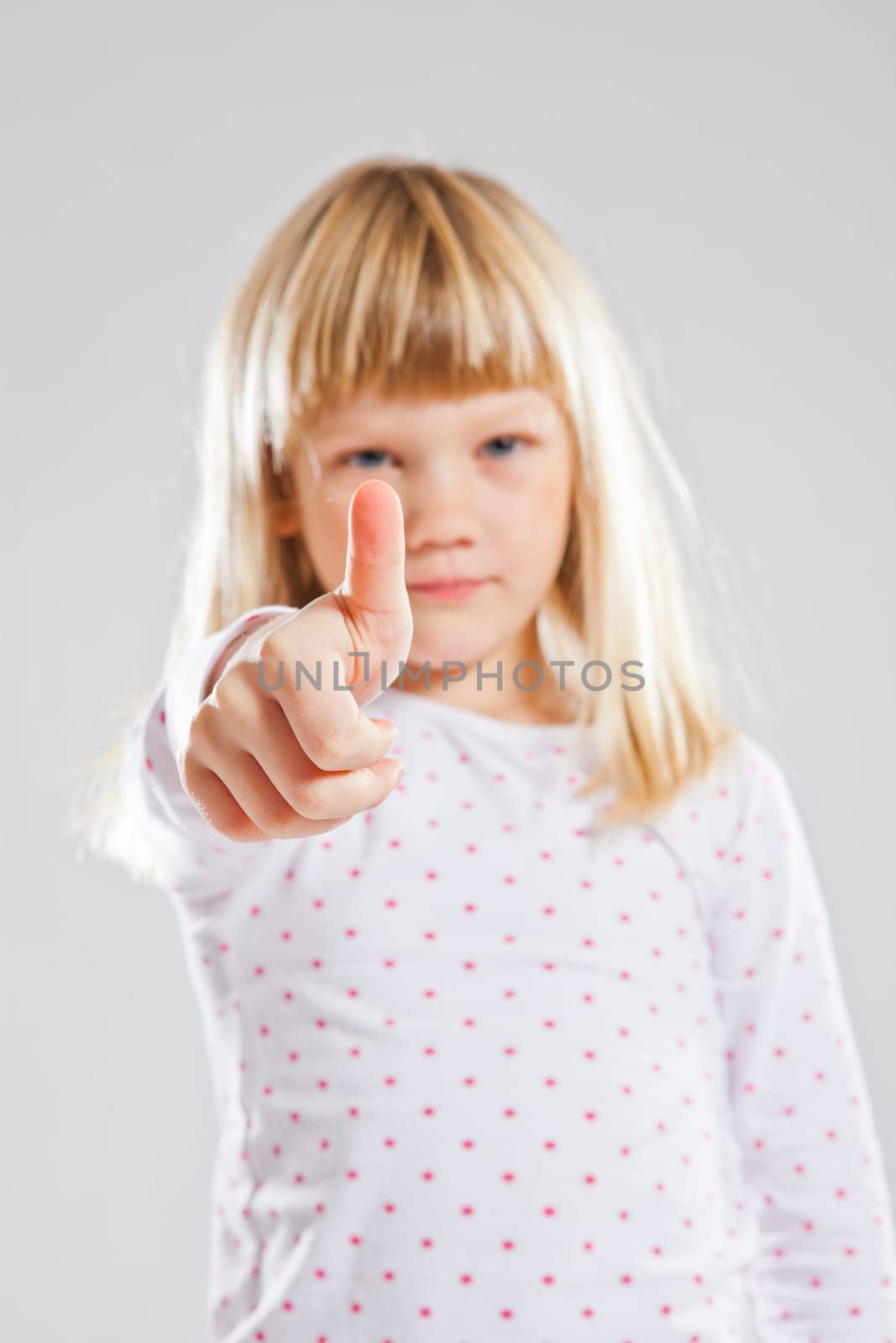 Studio portrait of serious looking young girl showing thumbs up or ok sign