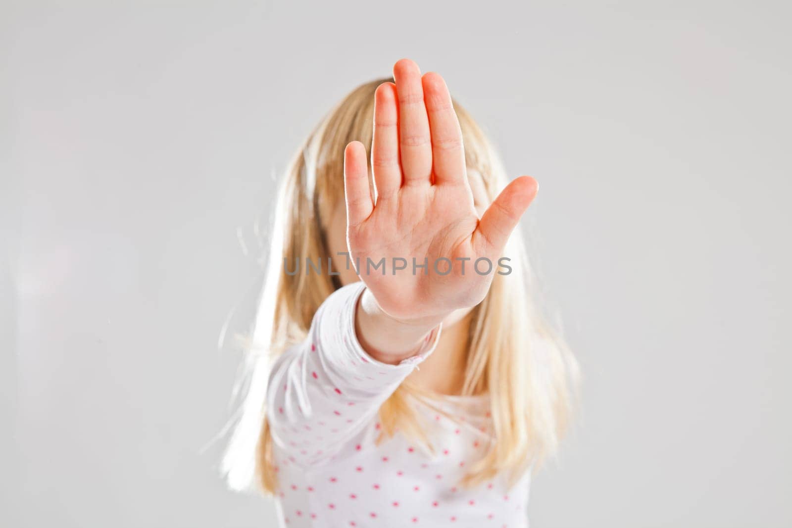 Studio portrait of young girl showing stop hand sign or signal in front of face