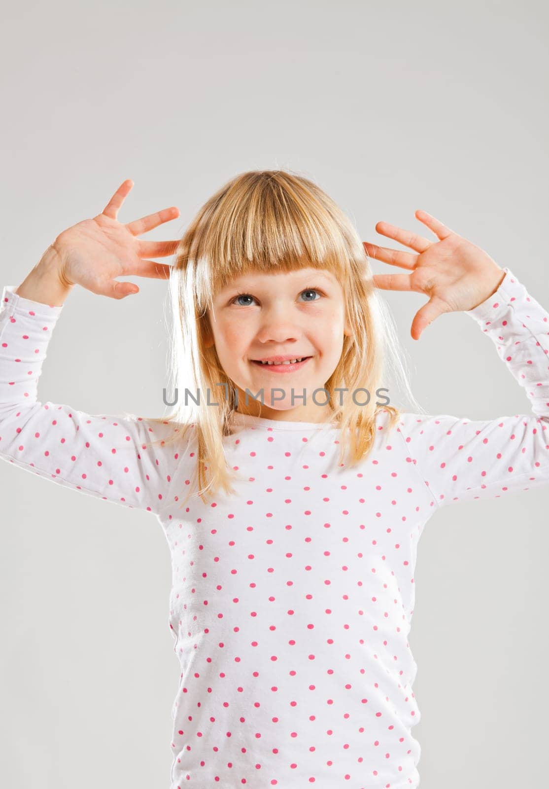 Studio portrait of happy smiling young girl looking upwards with raised hands