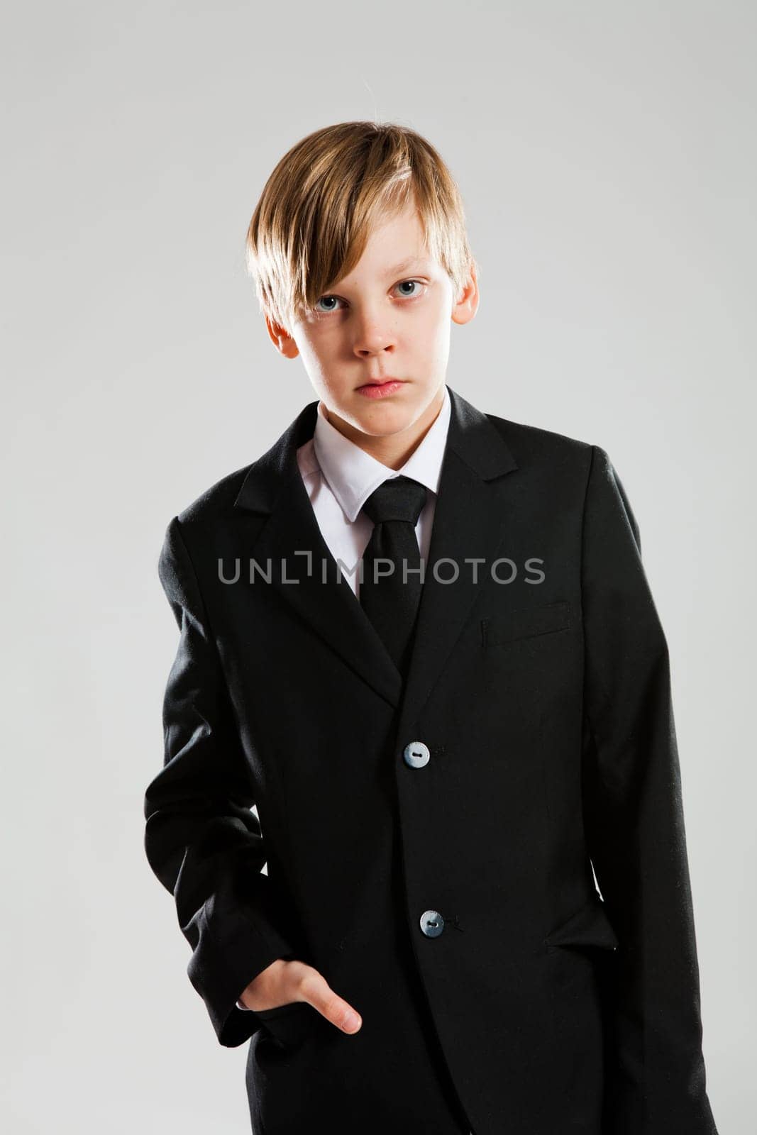 Studio portrait of serious looking young boy with hand in pocket of black suit