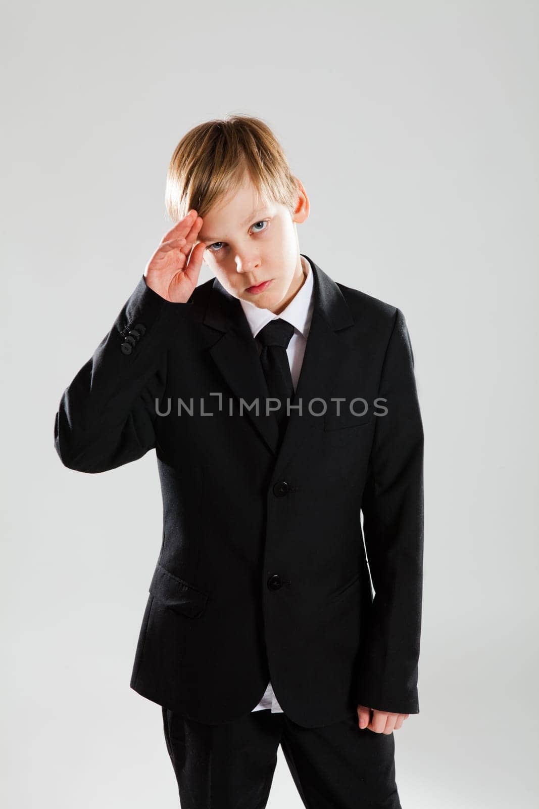 Studio portrait of serious looking young boy in black suit saluting