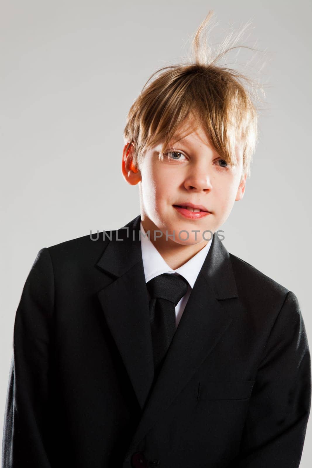 Studio portrait of smiling and relaxed young boy in black suit with wind blowing hair