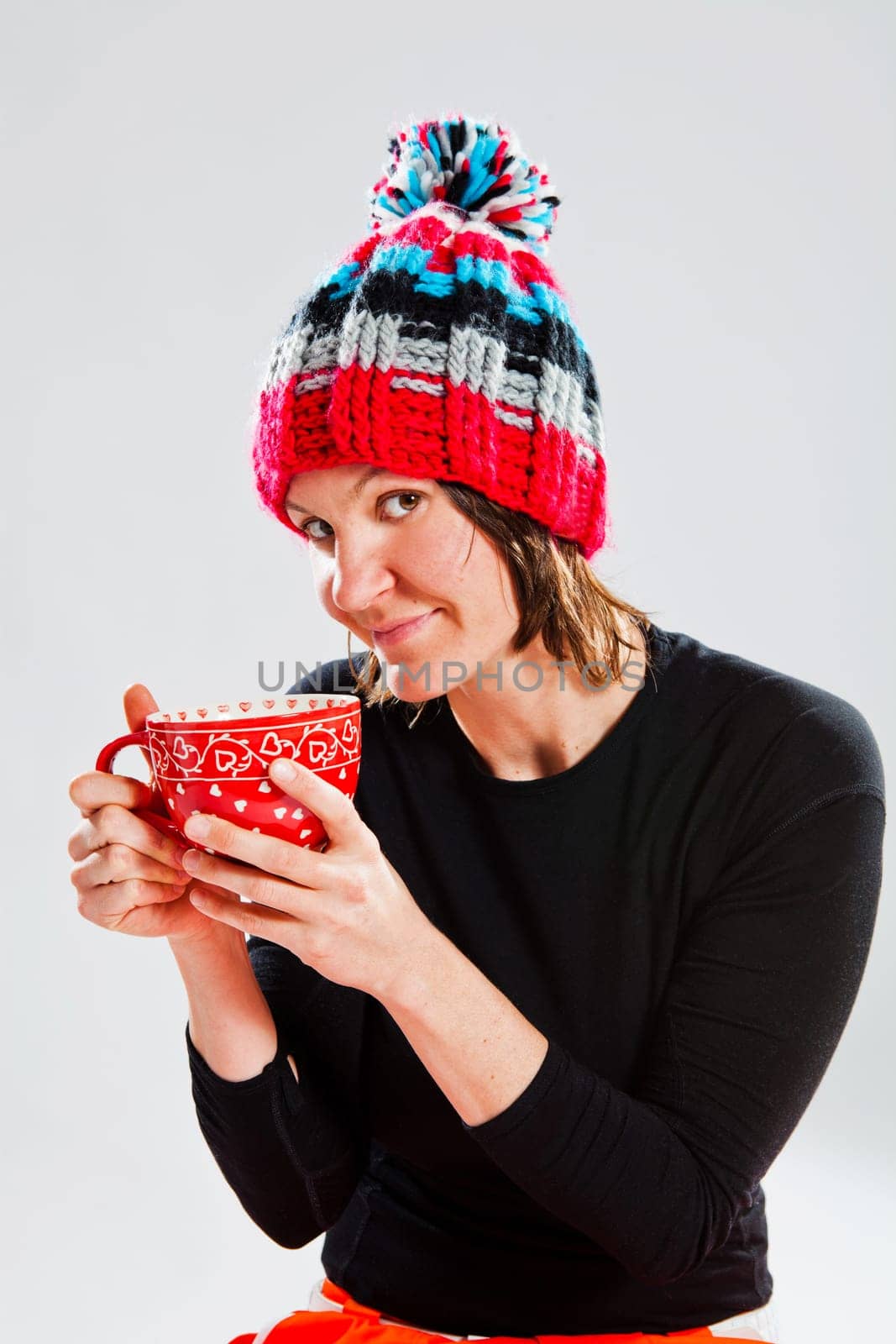 Studio portrait of smiling happy woman in knitted woollen hat holding large cup