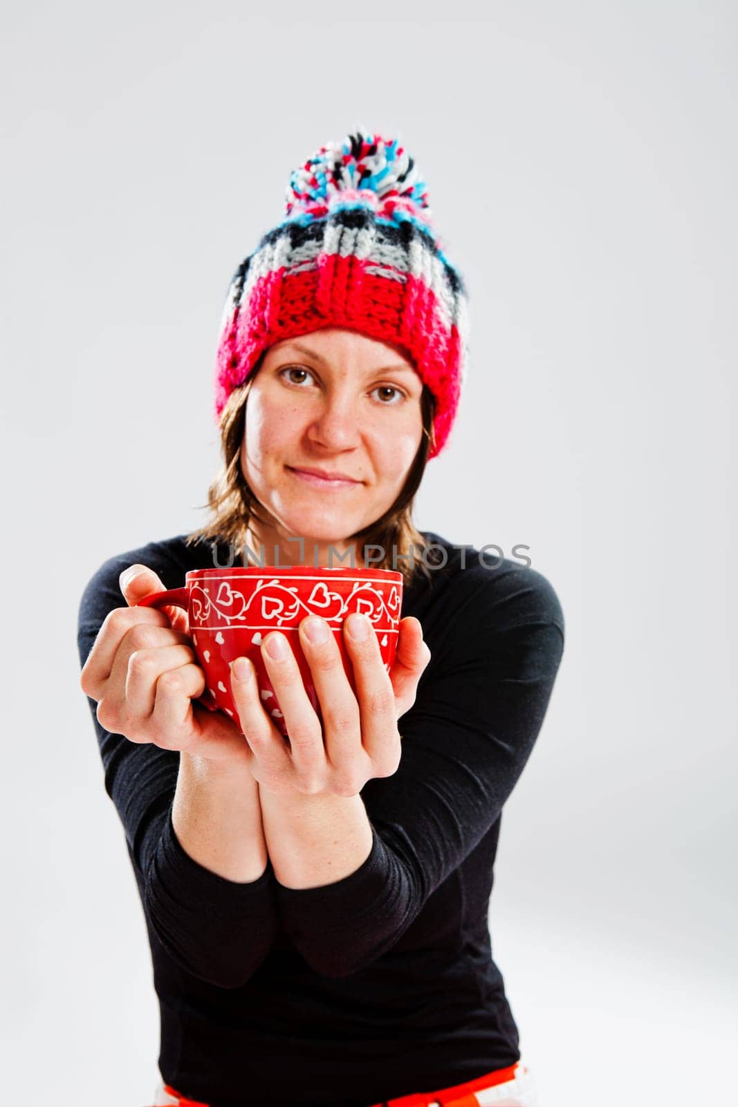 Studio portrait of smiling happy woman in knitted woollen hat holding large cup