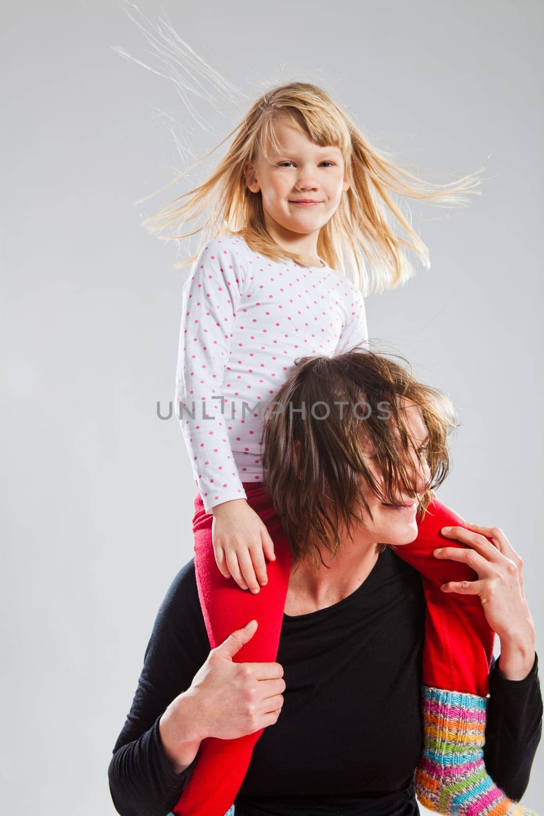 Studio portrait of happy woman carrying smiling young girl on shoulders