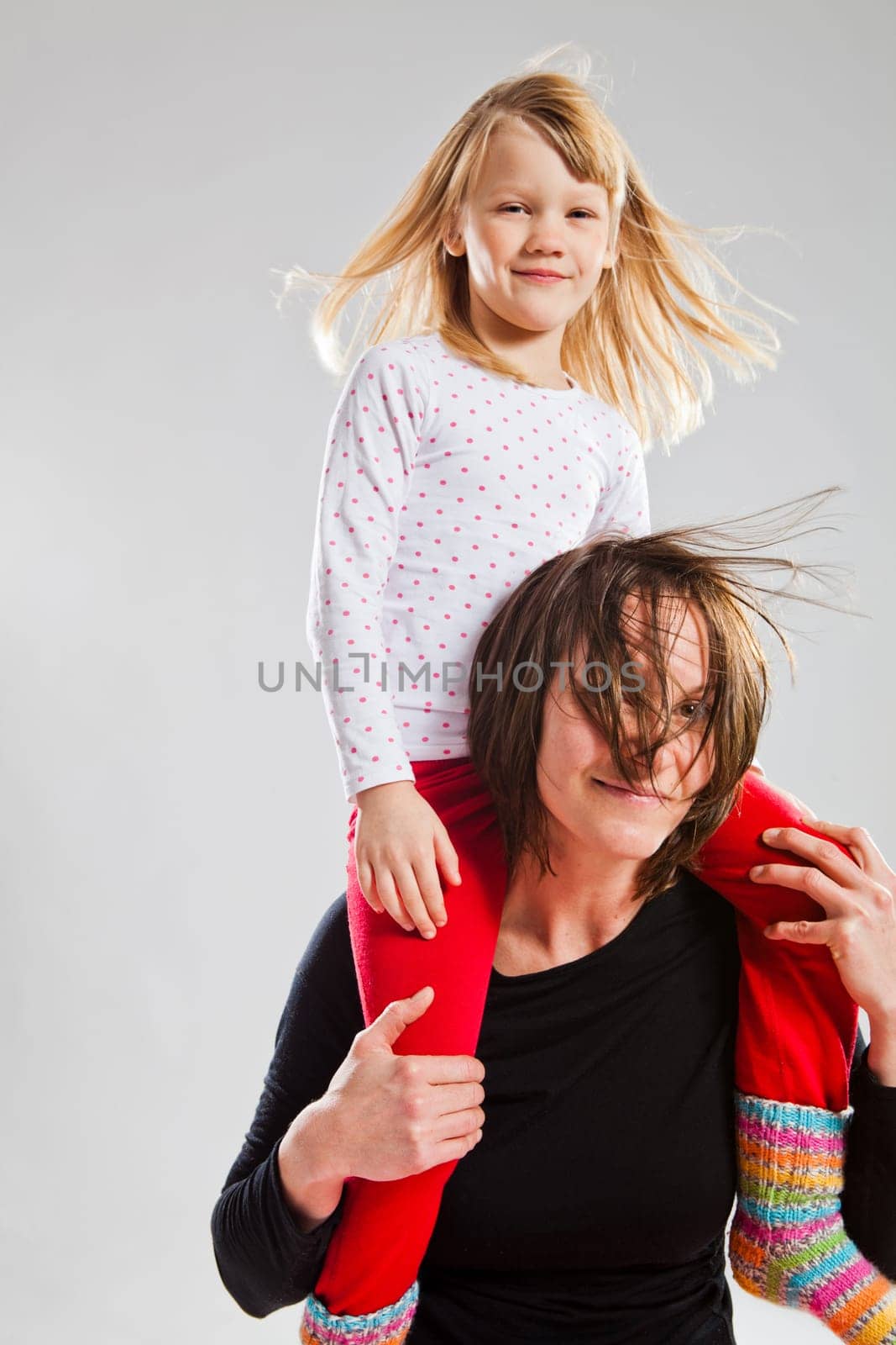 Studio portrait of happy woman carrying smiling young girl on shoulders