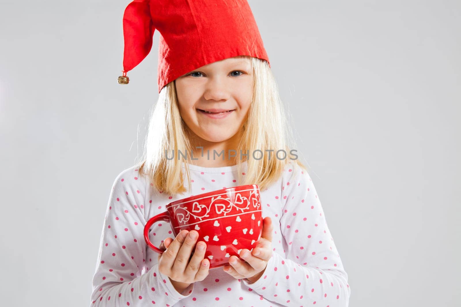 Studio portrait of happy young girl wearing red Christmas elf hat and holding a big red cup