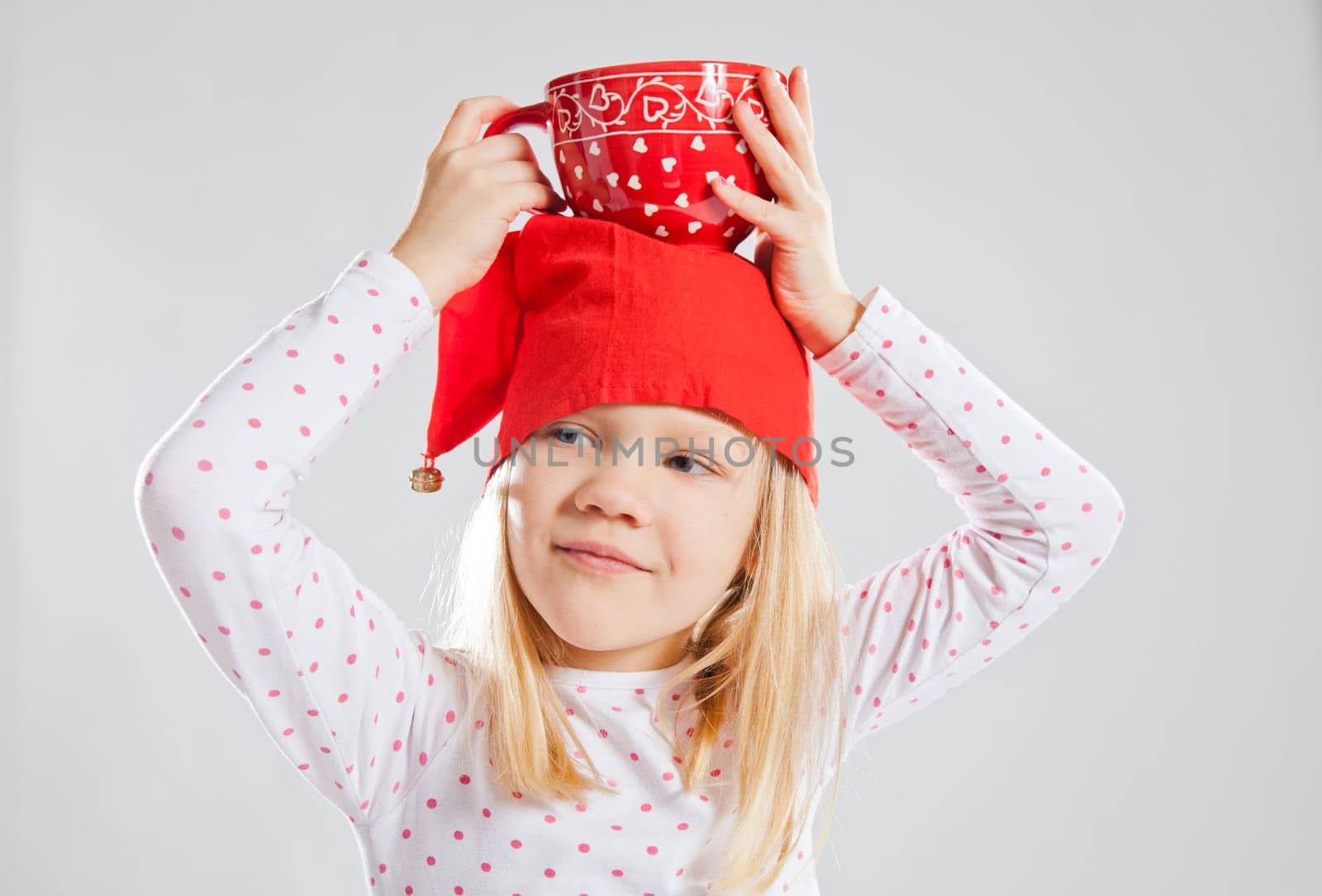 Studio portrait of smiling young girl wearing red Christmas elf hat holding big red cup on head