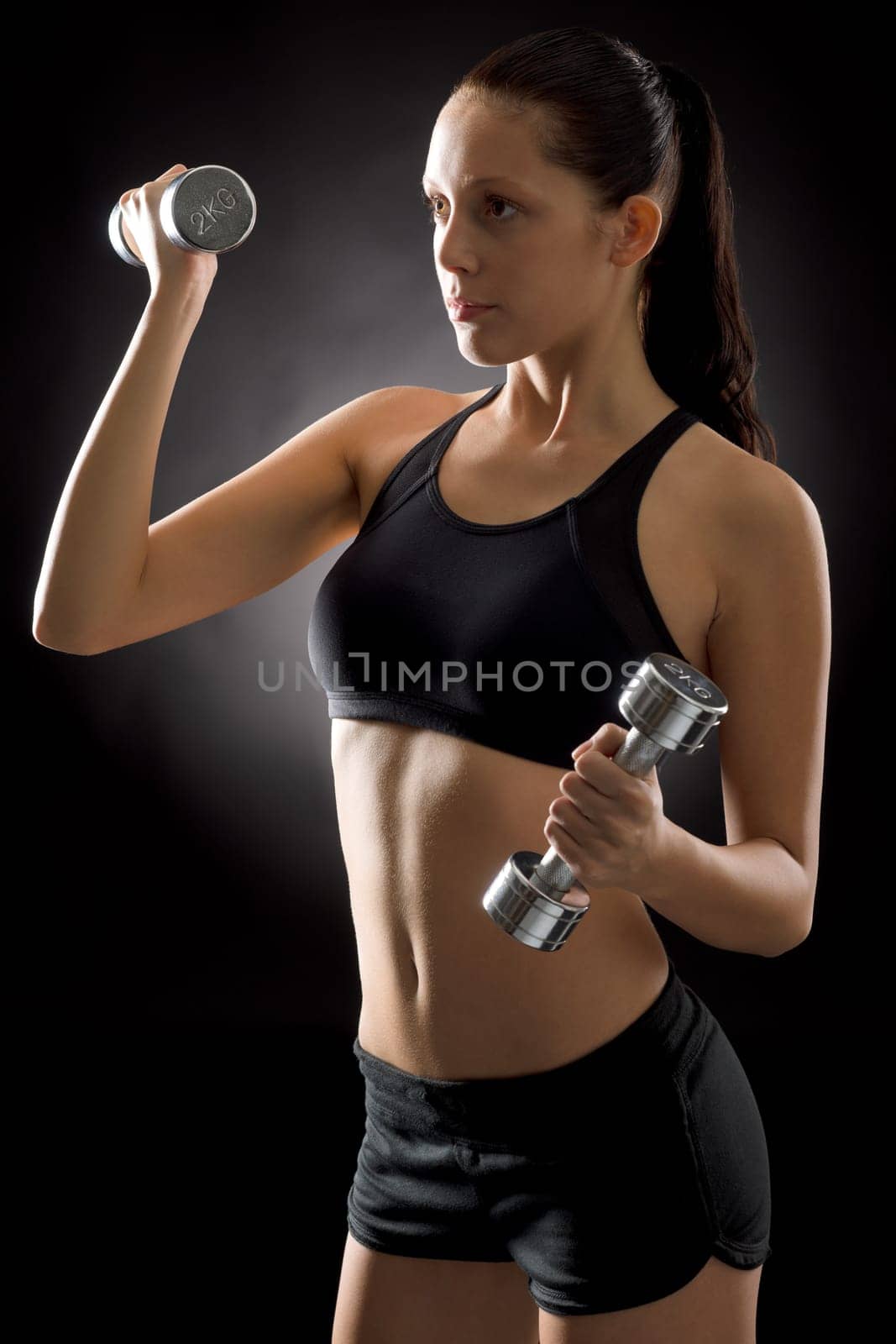 Sporty young woman holding dumbbells on black background