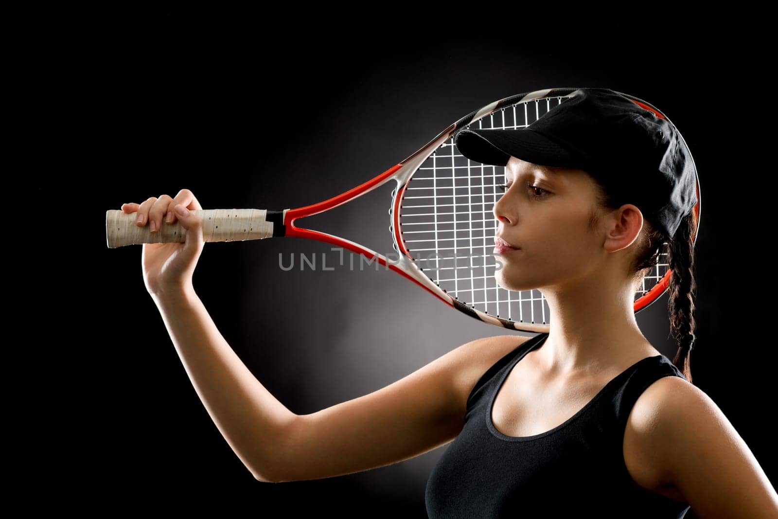 Young female tennis player posing with racket on black background