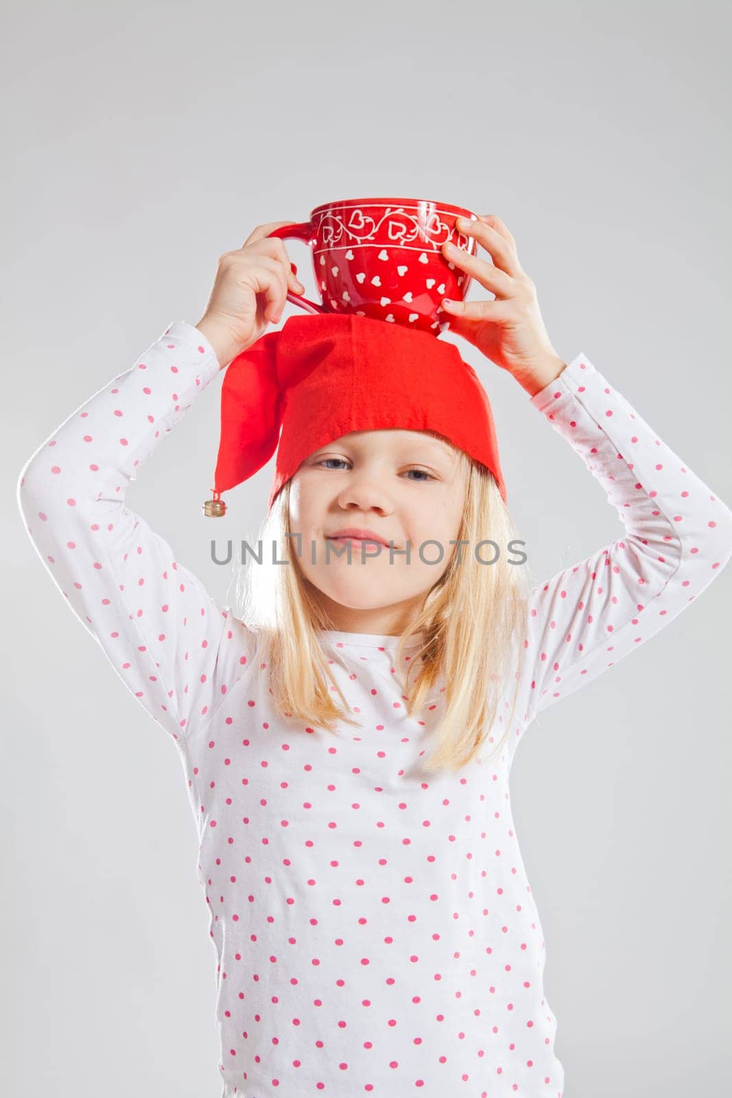 Studio portrait of smiling young girl wearing red Christmas elf hat holding big red cup on head