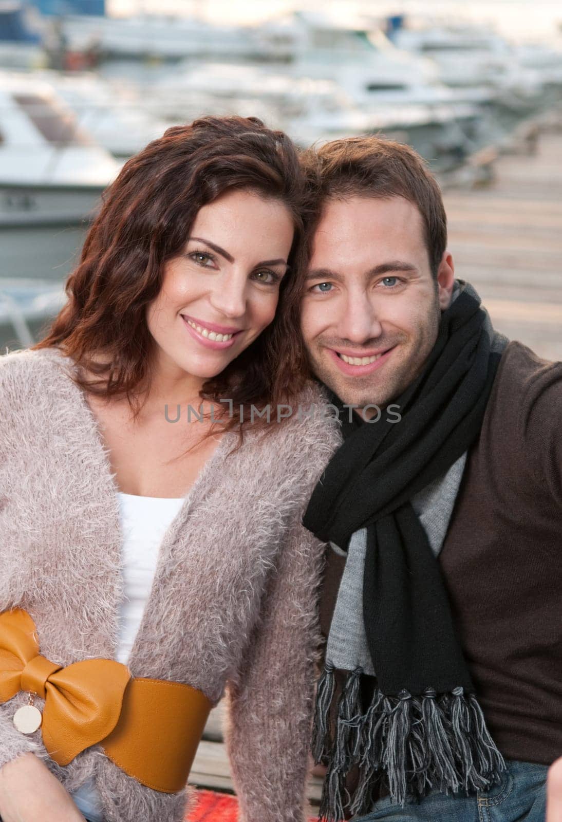 Beautiful couple in love sitting on wooden pier in marina