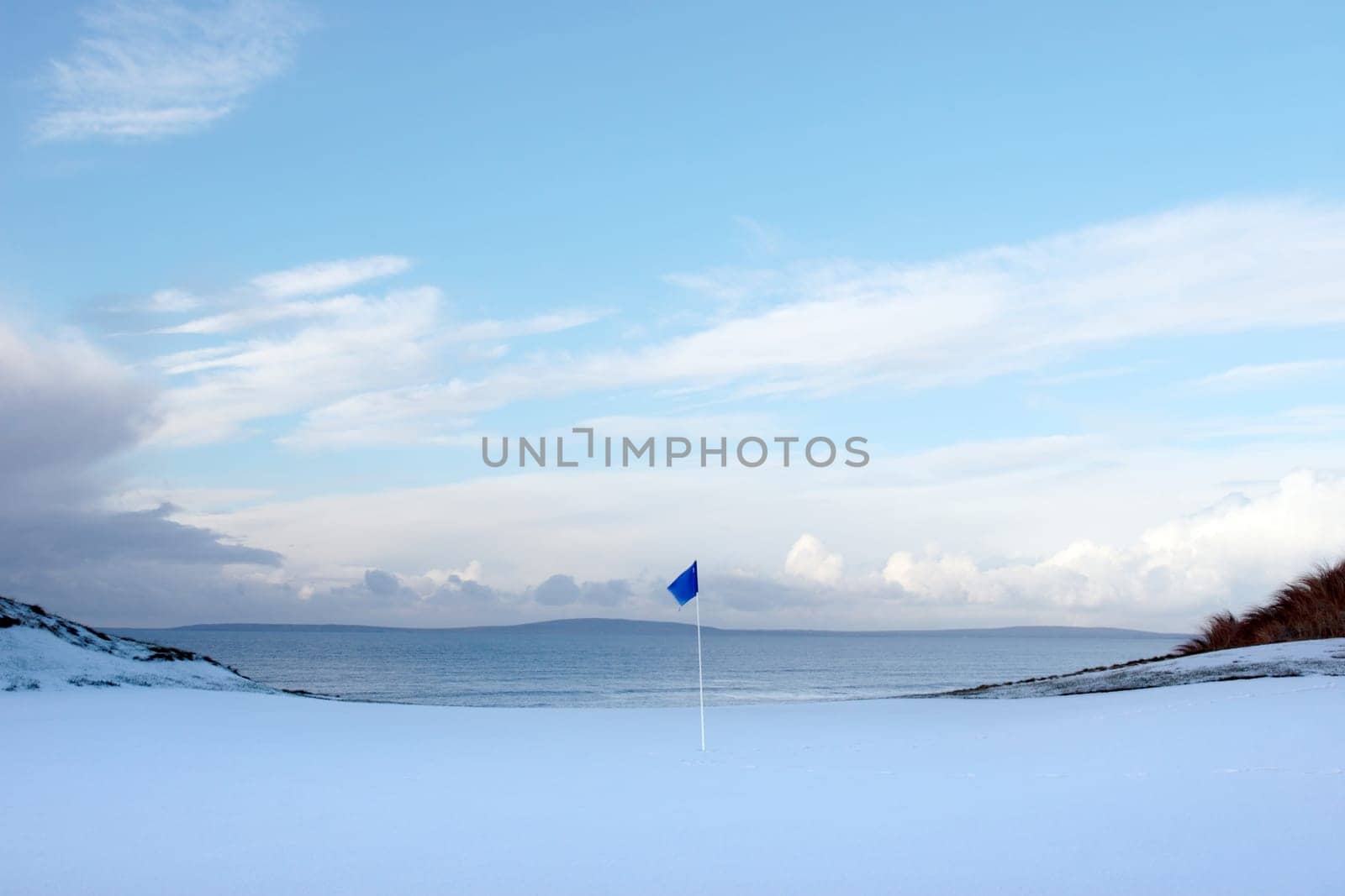 a snow covered links golf hole in ireland in winter evening weather with blue flag