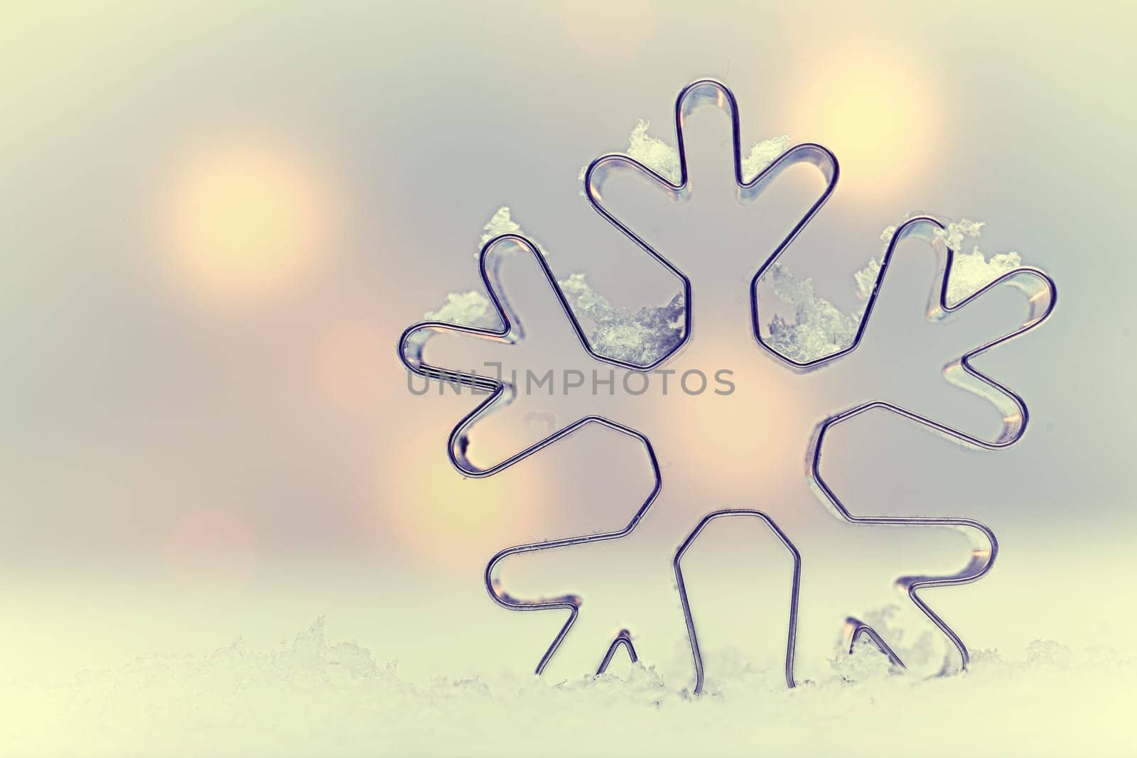 Ethereal snowflake Seasonal background with a snowflake-shaped metal cookie cutter oulined against soft muted Christmas lights with copysapce