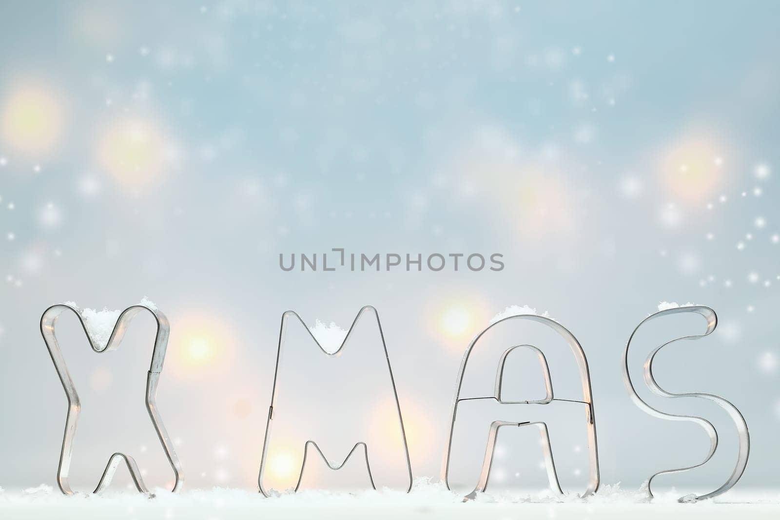 Metal Xmas cookie cutters standing in snow outlined against a soft blue atmospheric background with muted glowing lights and lots of copyspace for your Christmas greeting
