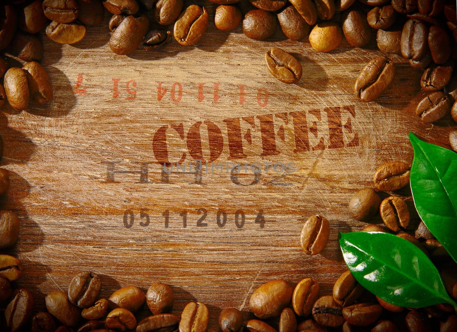 Fresh roasted coffee beans framing an old wooden board stamped with the word COFFEE and the shipment number of a consignment of beans with two fresh green leaves in the corner