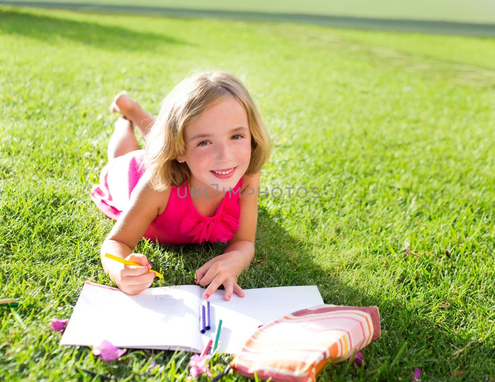 child kid girl doing homework smiling happy lying on grass garden with flowers