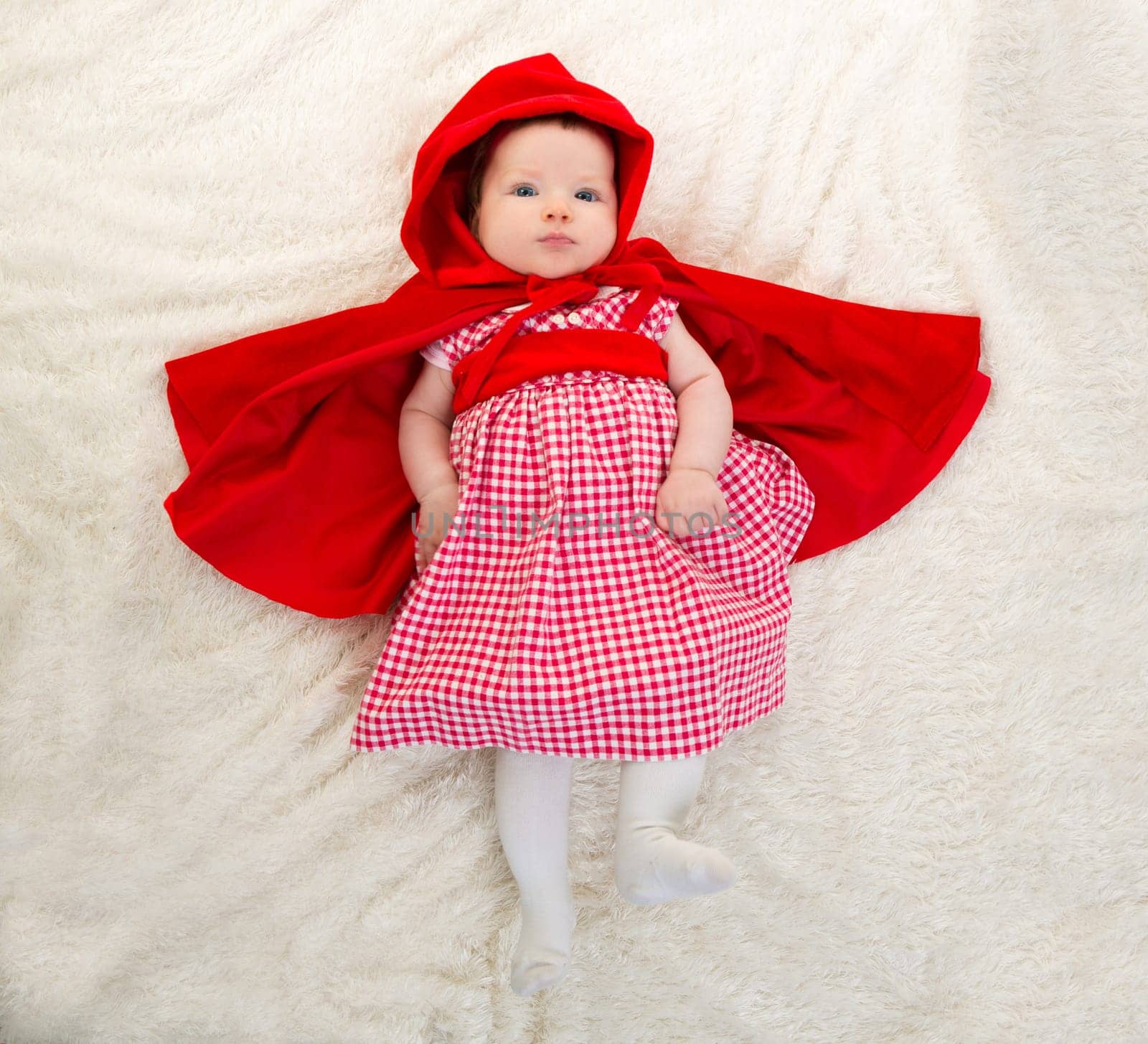 Baby Little Red Riding Hood on white fur lying with open cape