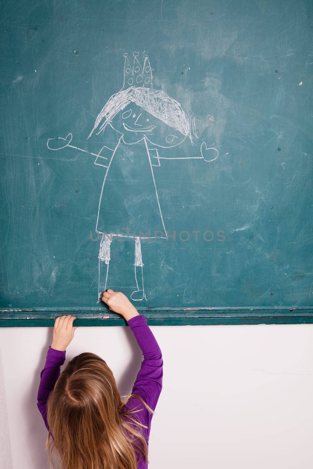 Studio portrait of young girl in classroom drawing image of princess with crown on a chalkboard