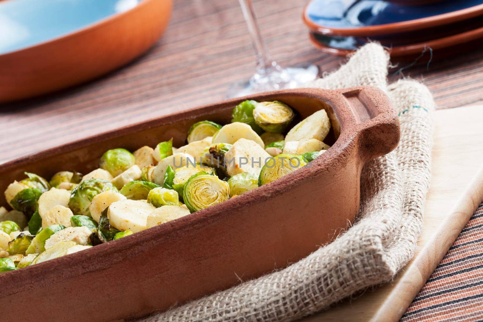 Roasted parsnips and brussel sprouts in terracota baking dish.