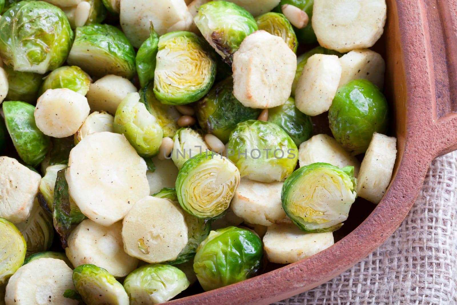 Roasted parsnips and brussel sprouts in terracota baking dish.