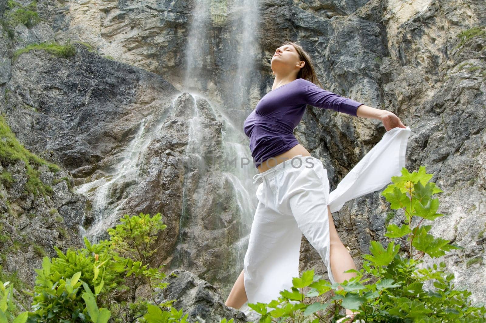 A young sporty woman exercising yoga exercises in front of a waterfall