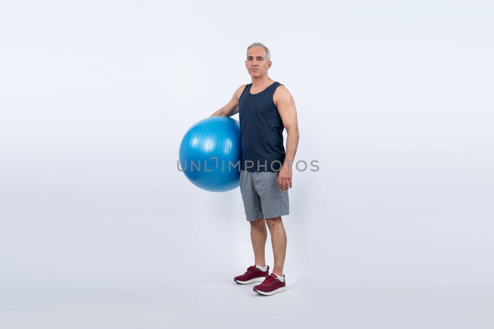 Full body length shot athletic and sporty senior man with fitness exercising ball in standing posture on isolated background. Healthy active and body care lifestyle after retirement. Clout