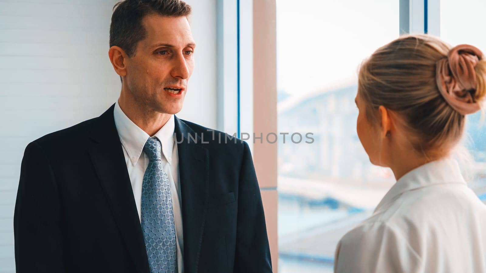 Two business people talk project strategy at office meeting room. Businessman discuss project planning with colleague at modern workplace while having conversation and advice on financial report. Jivy