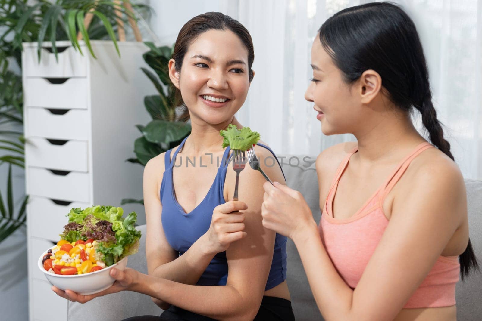 Young sporty Asian women in sportswear holding salad bowl together fill with vibrant of fruit and vegetable. Natural youthful and fit body lifestyle with balance nutrition and home exercise. Vigorous